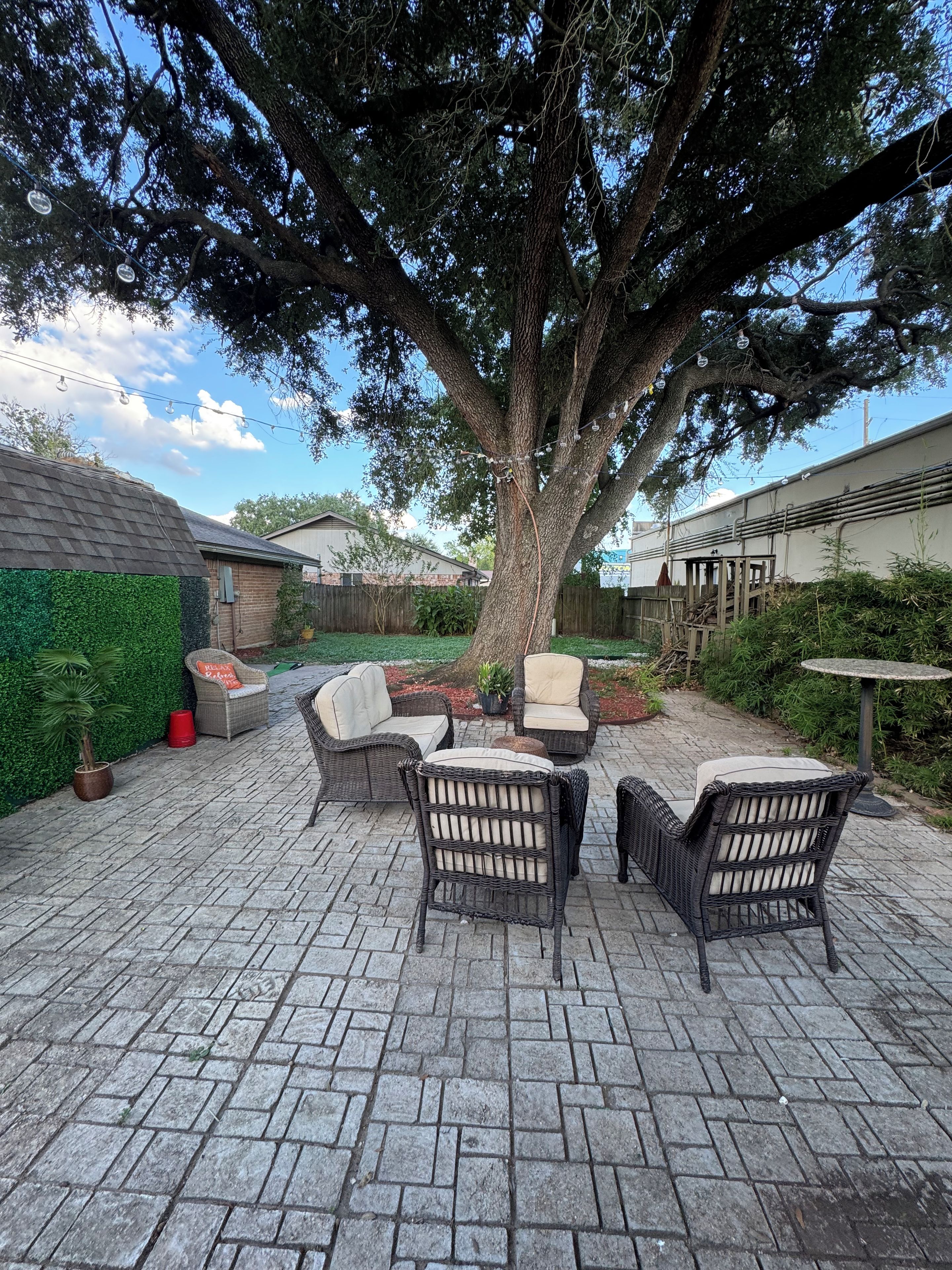 A patio area with outdoor furniture, a large tree, and a brick floor.