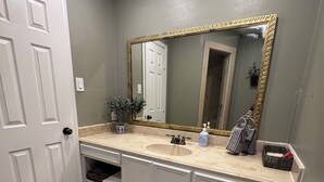 A bathroom with a white door, a large mirror with a gold frame, a sink, and a towel rack. - Fabulous 3-bedroom house with AC in vibrant Houston suburban neighborhood. (Houston)