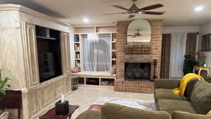 A living room with a sofa, television, fireplace, ceiling fan, and a bookshelf. - Fabulous 3-bedroom house with AC in vibrant Houston suburban neighborhood. (Houston)