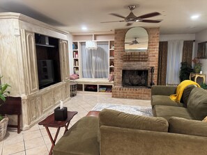 Ein Wohnzimmer mit einer Couch, einem Fernseher, einem Kamin, einem Deckenventilator und einem Bücherregal.