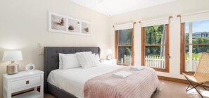 Ein Schlafzimmer mit einem Bett, Nachttischen, einem Sessel und einem Fenster mit Blick auf Grünflächen.