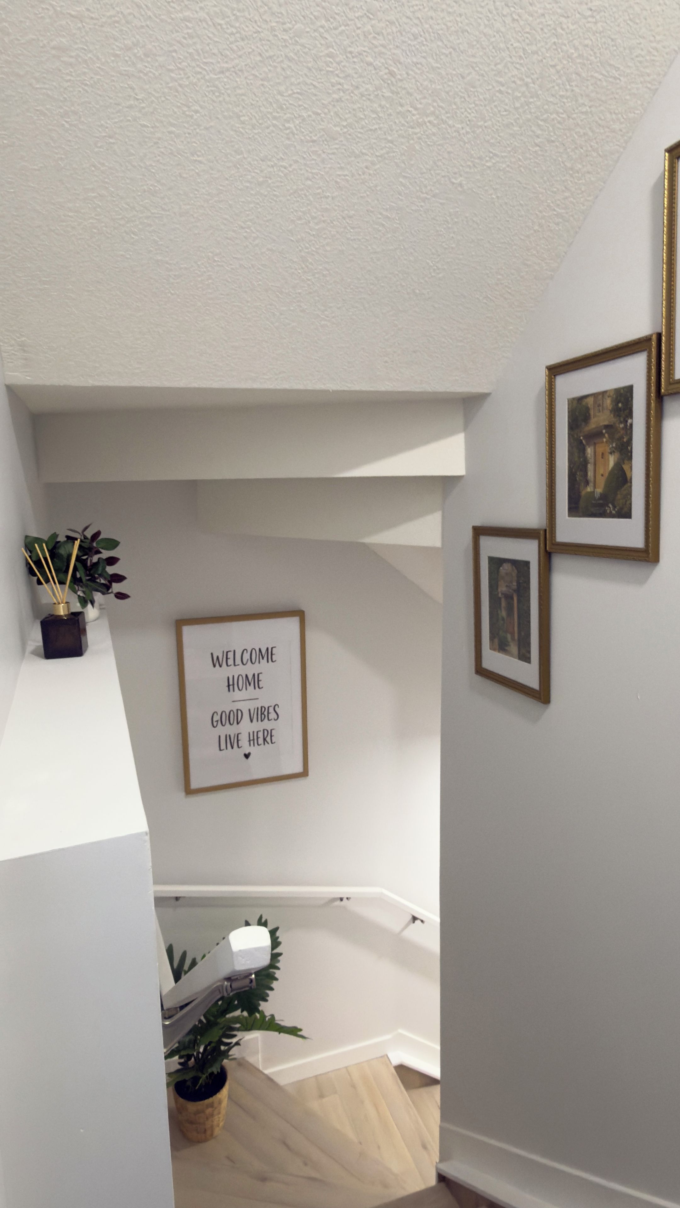 Una escalera con un letrero de bienvenida, cuadros enmarcados y una planta en maceta.