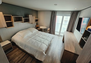 Habitació d'hotel moderna amb un llit gran, prestatges integrats, una taula petita i un balcó amb cortines.