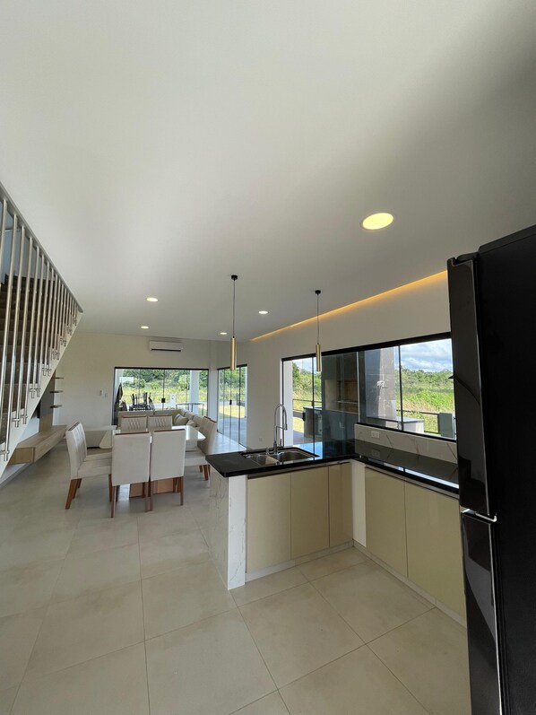 A modern kitchen with a central island, a dining area with a sofa and chairs, and a staircase leading to an upper level.