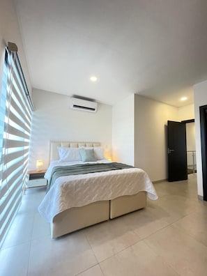 A modern bedroom with a large bed, bedside tables, an air conditioning unit, and a door.
