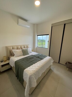 A bedroom with a bed, bedside table, lamp, and a window with a view.