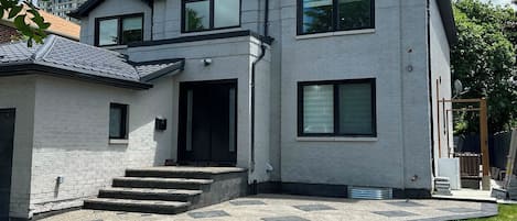 Una casa moderna de dos pisos con fachada de piedra, entrada principal con escalones y un césped bien cuidado.