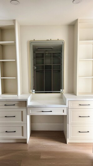 A room with a built-in desk, a wardrobe with multiple shelves, and a large mirror.