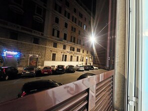 Un hôtel à la façade classique, avec de nombreuses voitures garées devant et une rue illuminée la nuit.