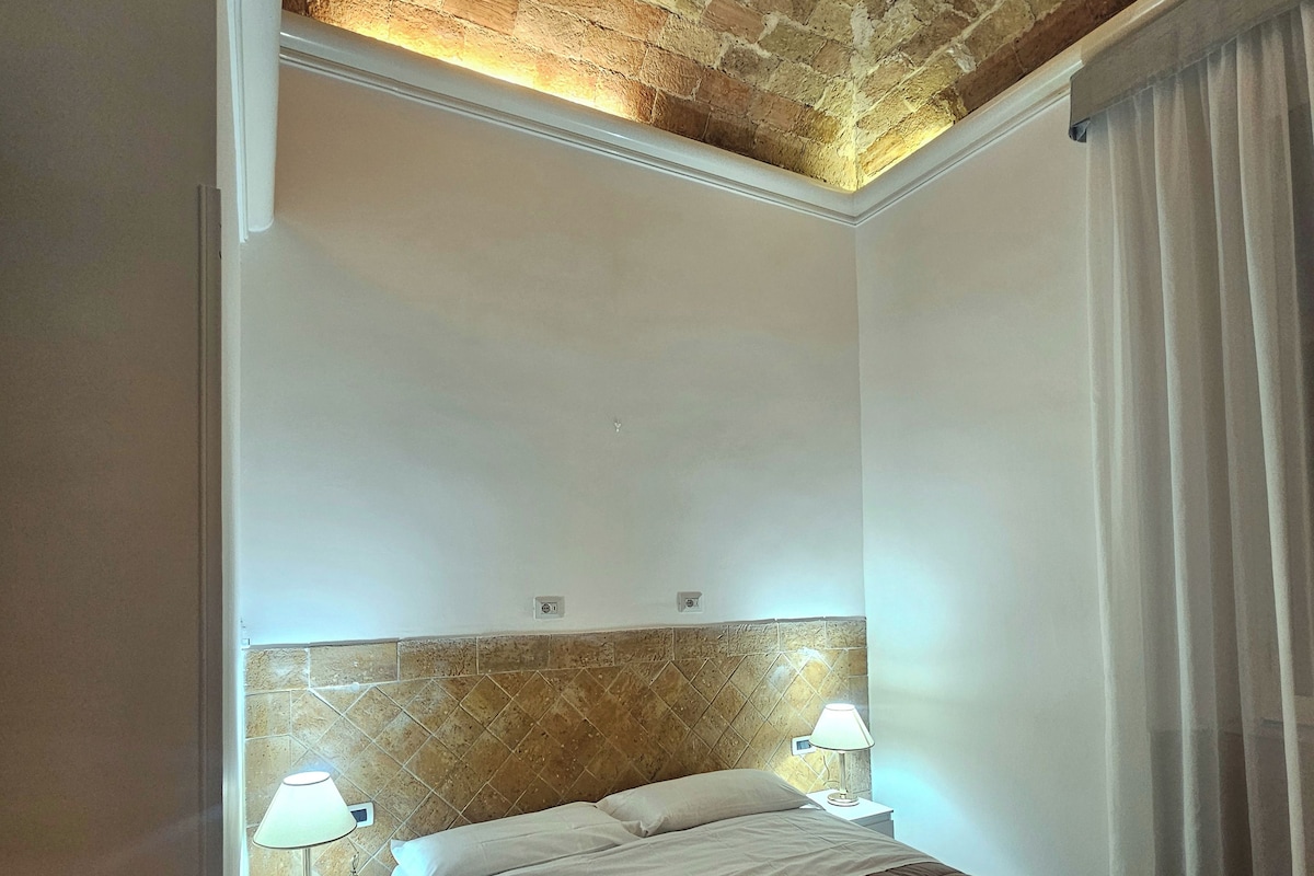 Une chambre d’hôtel avec un plafond en briques, un lit avec une literie marron, deux lampes de chevet et une fenêtre avec des rideaux.