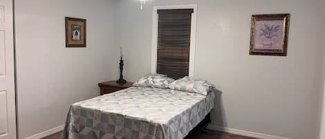 A bedroom with a bed, a nightstand, a ceiling fan, a window with blinds, and two framed pictures on the wall.