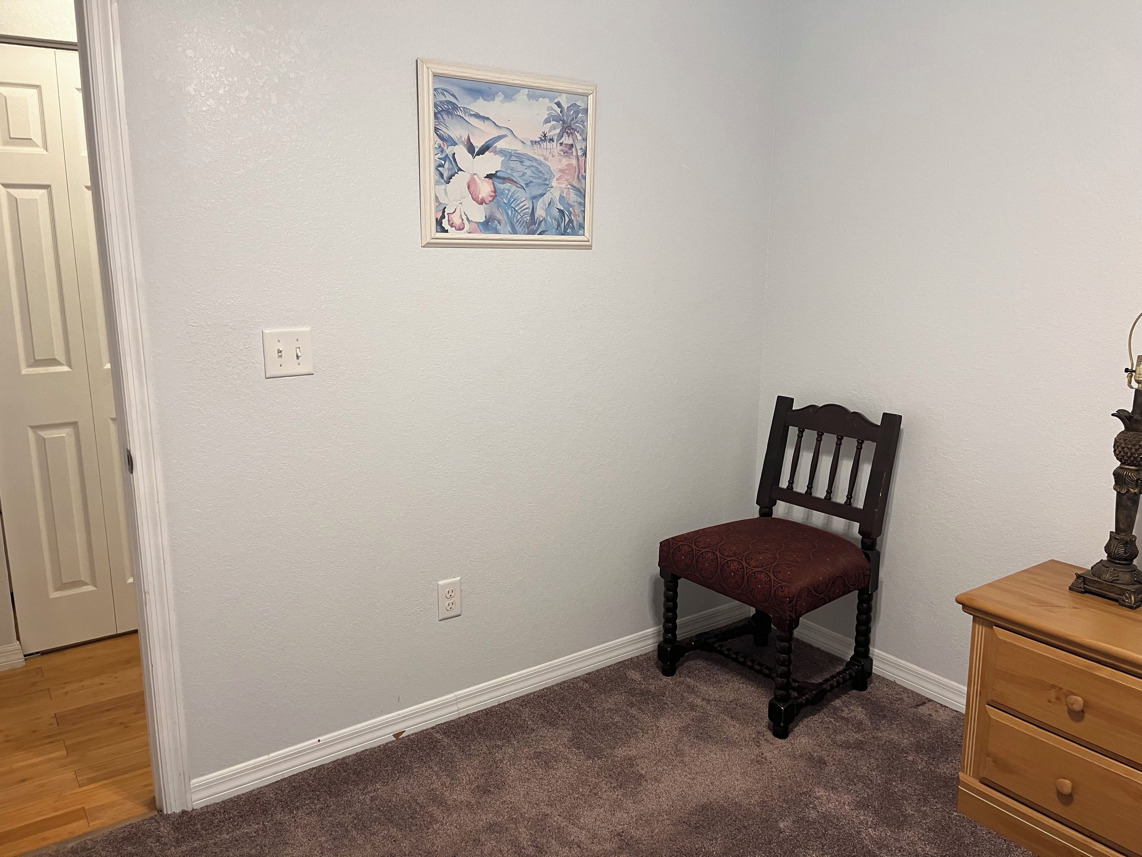 Ein Zimmer mit einem Sessel, einem Schminktisch und einem an der Wand hängenden Gemälde.