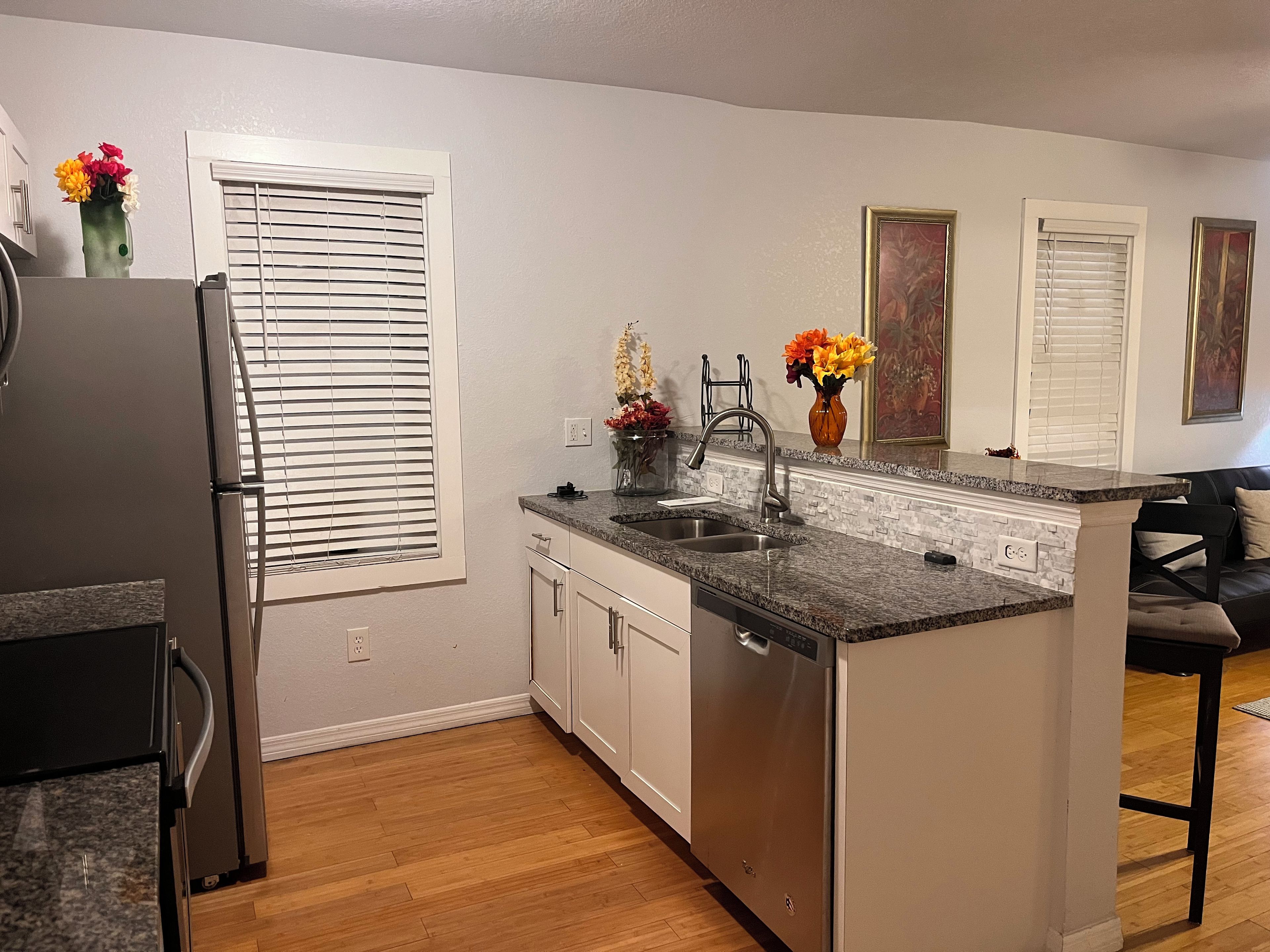 A kitchen with a built-in dishwasher, a refrigerator, and a window with blinds.