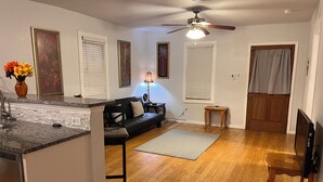 Un espacio habitable compacto con kitchenette, un sofá negro, una mesa de comedor de madera y un ventilador de techo.