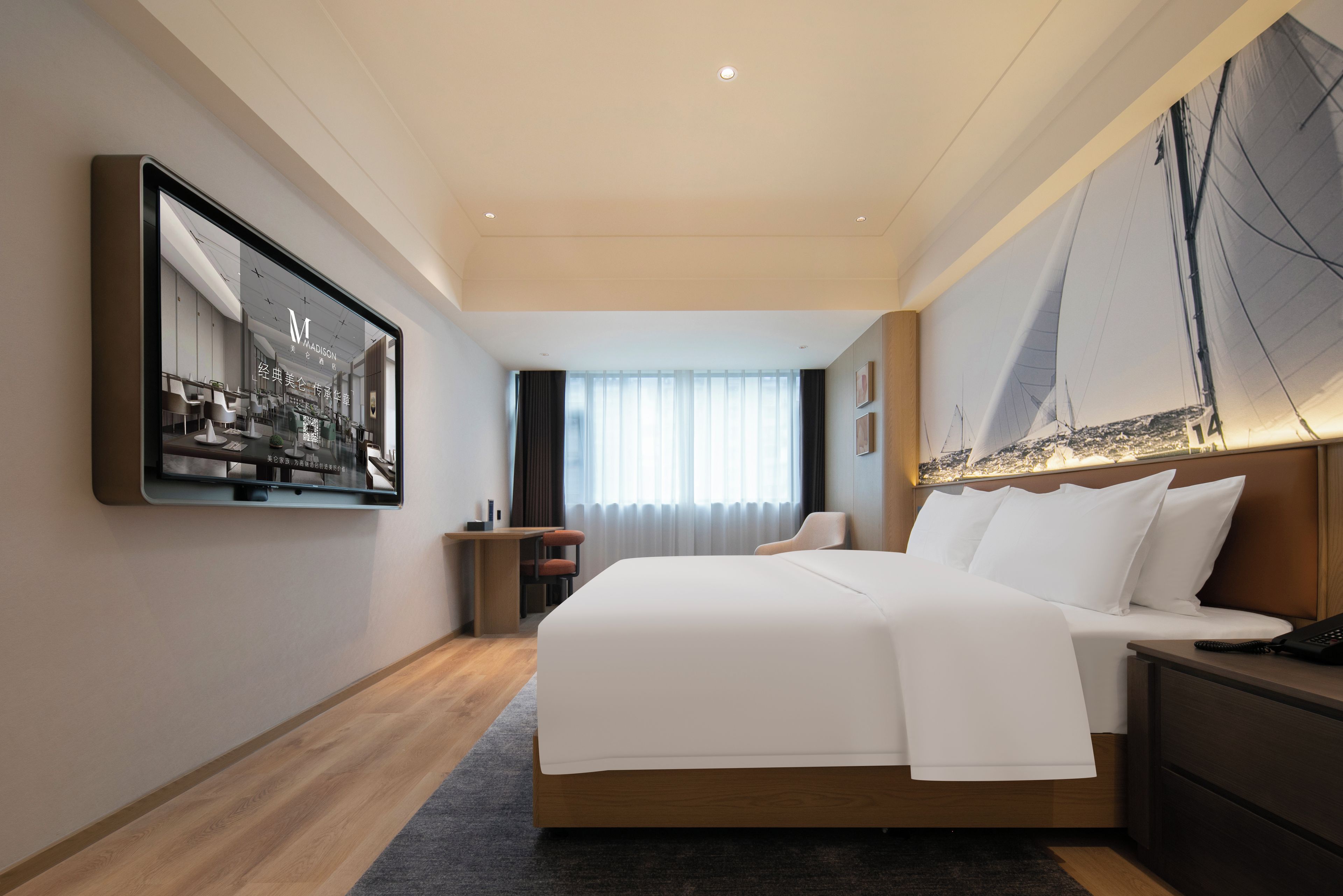 Habitación de hotel con una cama grande, un escritorio y una silla. Cuenta con un ventanal con cortinas, un cuadro en la pared y vistas a un velero.