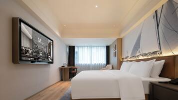 Habitación de hotel con una cama grande, un escritorio y una silla. Cuenta con un ventanal con cortinas, un cuadro en la pared y vistas a un velero.