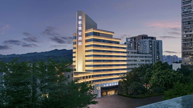 Un moderno edificio de hotel con un letrero vertical llamativo, varios pisos y una entrada bien iluminada.