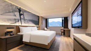 Habitación de hotel moderna con una cama grande, un escritorio, una silla, un televisor y una obra de arte colgada en la pared.