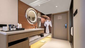 A hotel bathroom with a vanity, mirror, towel rack, and a robe hanging on the wall.