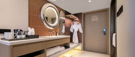 A hotel bathroom with a vanity, mirror, towel rack, and a robe hanging on the wall.