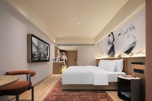 Una habitación de hotel moderna con una cama grande, un escritorio, una silla, una mesita de noche y un televisor montado en la pared.