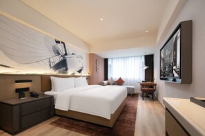 Quarto de hotel moderno com uma cama grande, uma escrivaninha e uma televisão.