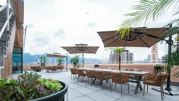 An outdoor seating area with tables and chairs, umbrellas, and potted plants.