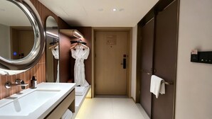 Un baño de hotel con un espejo grande, un lavamanos, una bata colgada en un perchero y un tendedero para toallas.