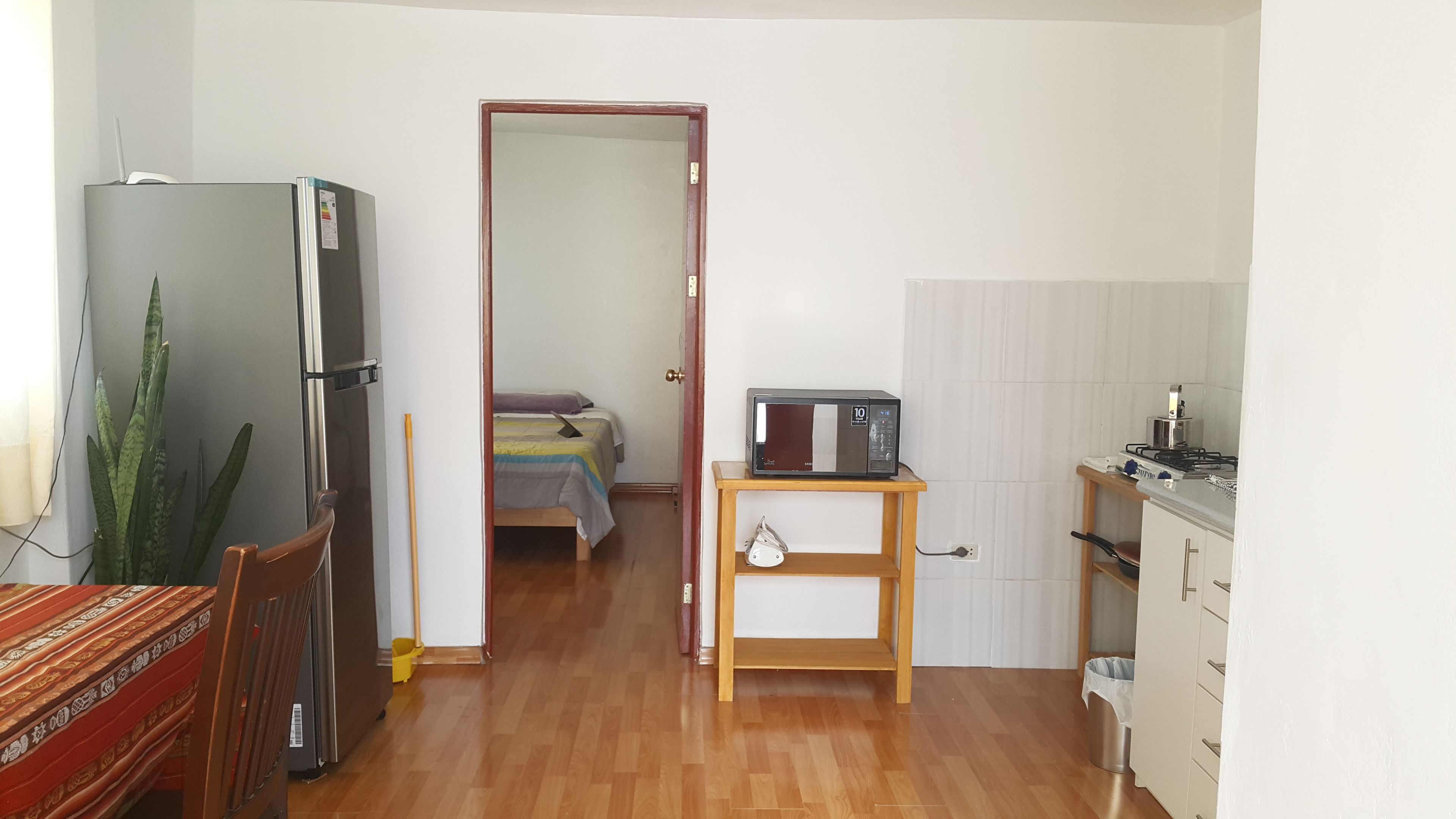 A compact living space with a kitchenette, a bed, a refrigerator, and a dining area.