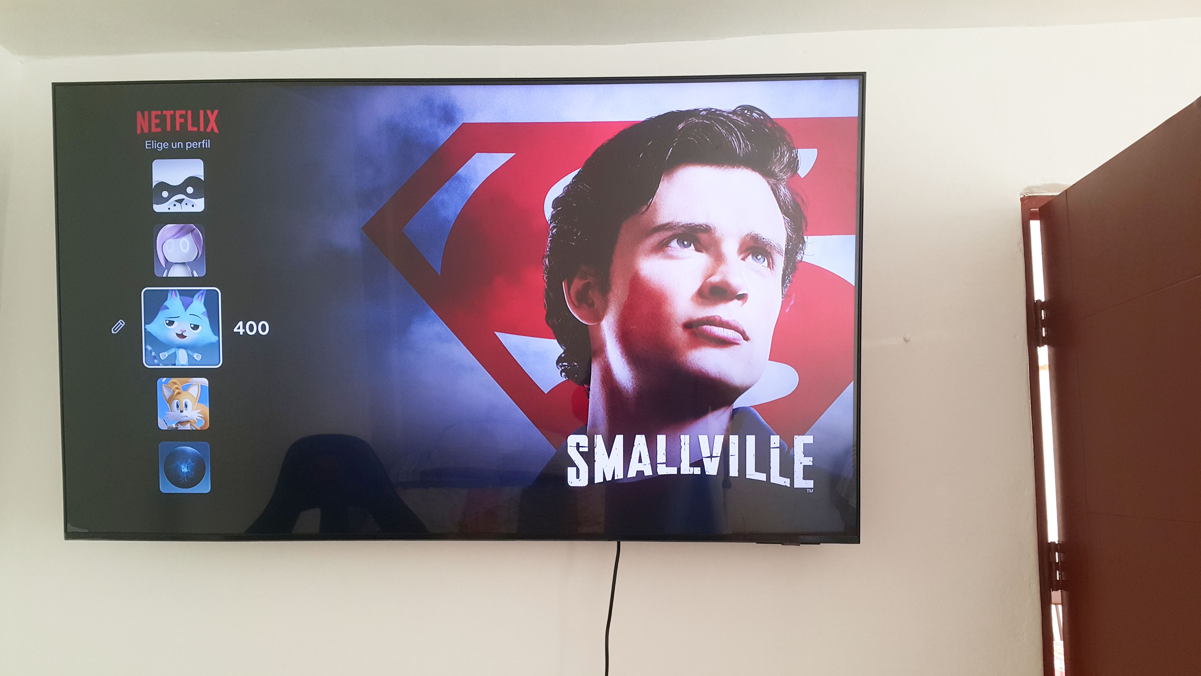 Un televisor mostrando una película con el logotipo de un superhéroe y el título 'SMALLVILLE'.