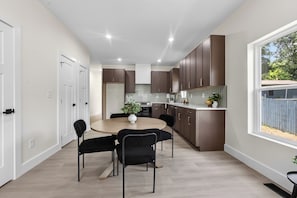 Une cuisine moderne avec des meubles de couleur brun foncé, une table de salle à manger ronde entourée de quatre chaises, et une fenêtre donnant sur l’extérieur.