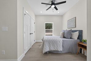 Ein Schlafzimmer mit einem Bett, Deckenventilator, Fenster und Tür.