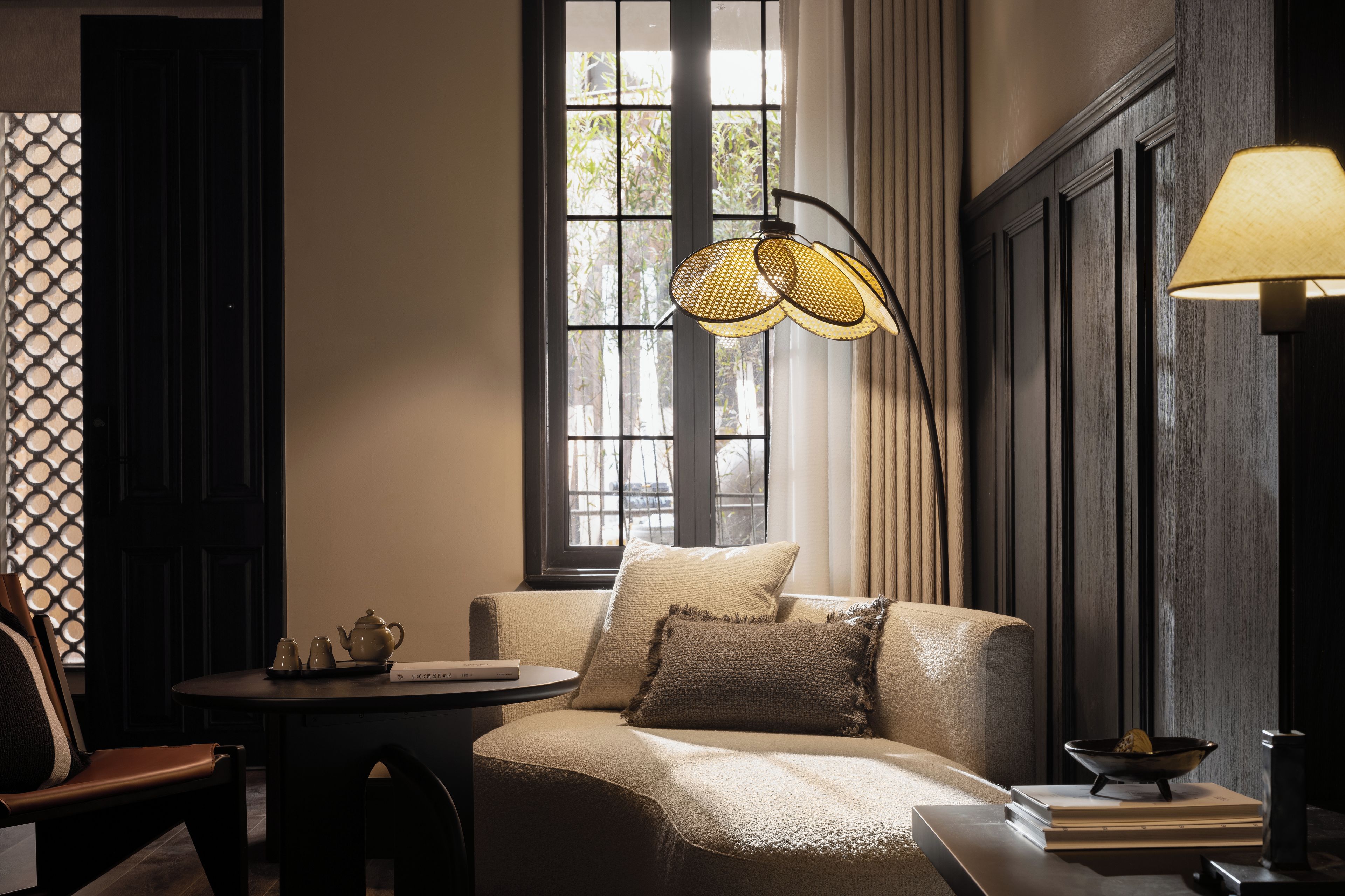 A cozy room with a sofa, a table with a teapot, a lamp, and a window with curtains.