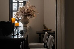 A dining area with a piano, a vase with dried flowers, a candle, and a fruit bowl.