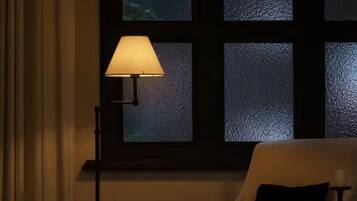 Quarto com uma cadeira, uma mesa, uma janela com vidro fosco e um abajur.