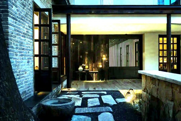 A courtyard with a stone pathway, a wooden bench, and a table with a lamp.
