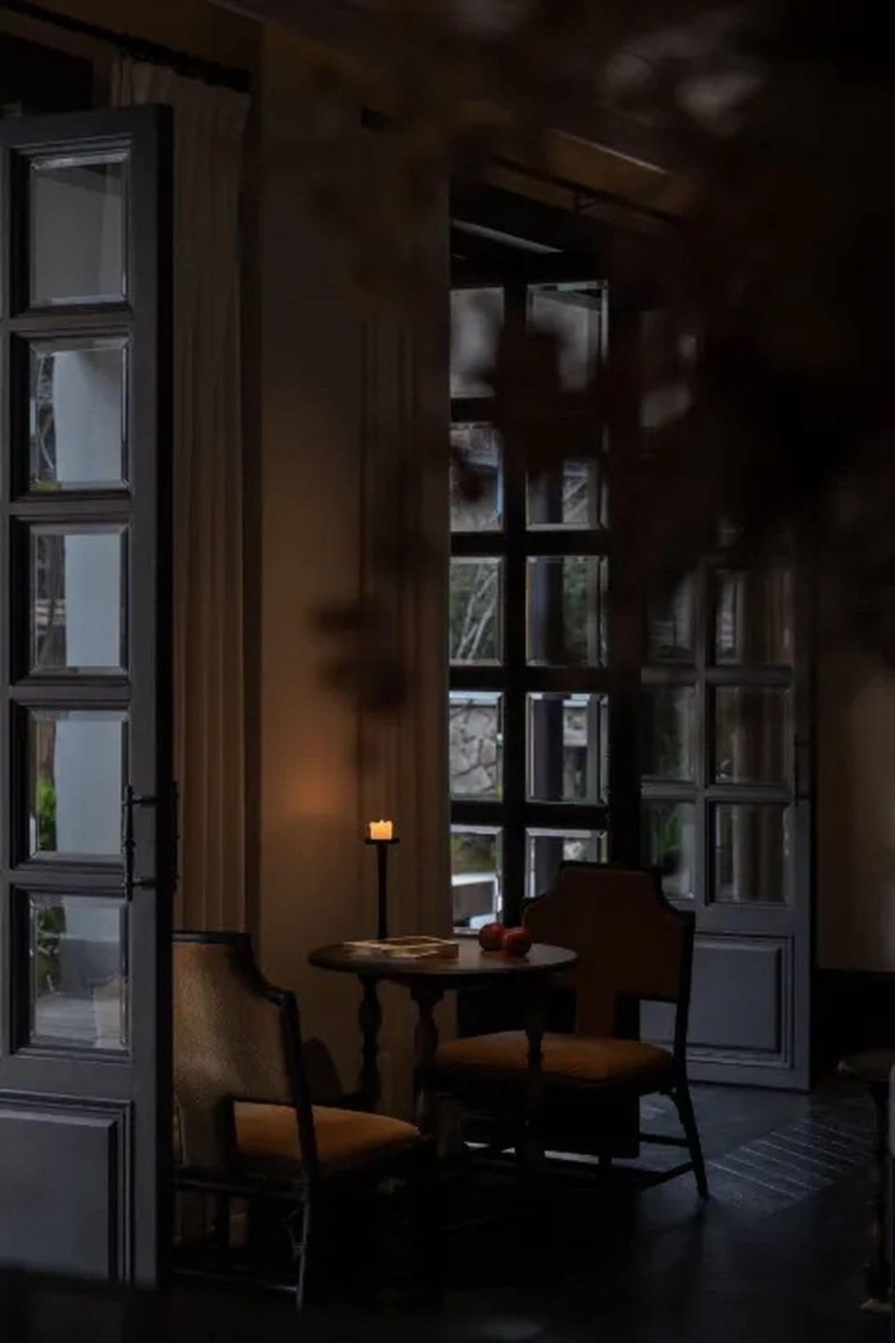 A room with a large window, a table with chairs, and a candle on the table.