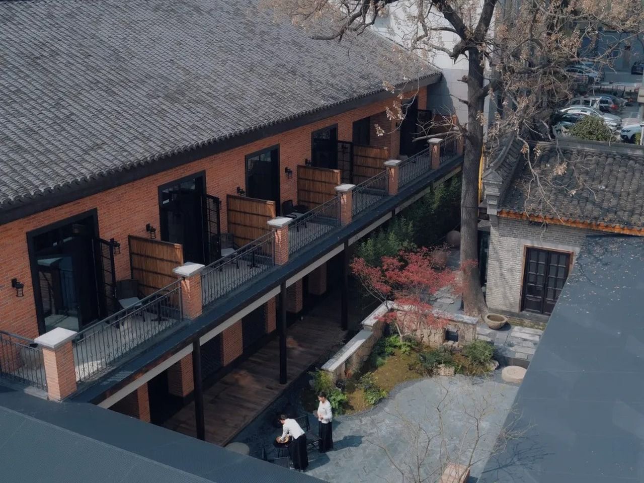 A two-story building with a brick facade, a balcony, and a small garden area.
