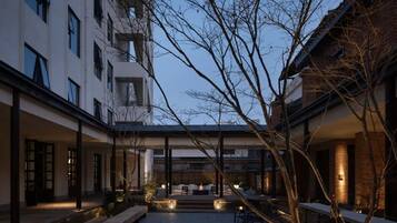 A courtyard with a covered seating area, a fire pit, and a view of a modern building.