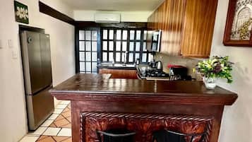 A kitchen with a central island, two bar stools, a refrigerator, and wooden cabinets.