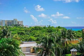A resort with lush greenery, a clear blue sky, and a view of the ocean.