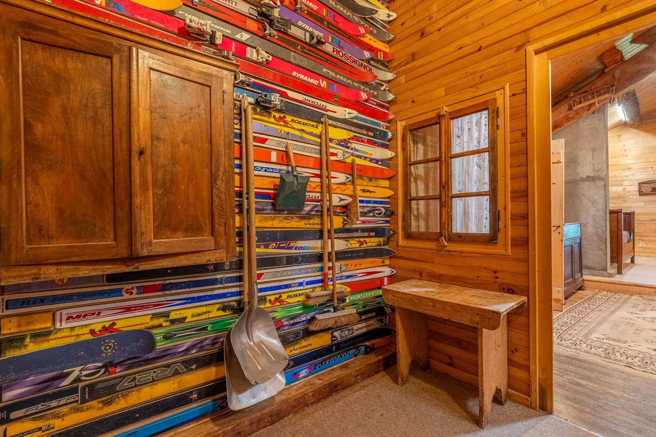 Een kamer met houten wanden, een houten bankje en een wandrek met diverse ski's.
