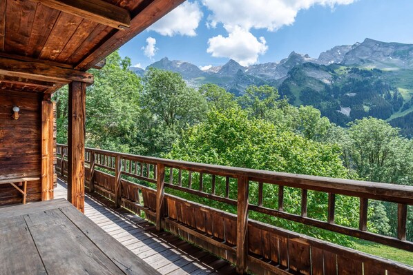 Eine Holzterrasse mit Geländer, die auf eine gebirgige Landschaft blickt.
