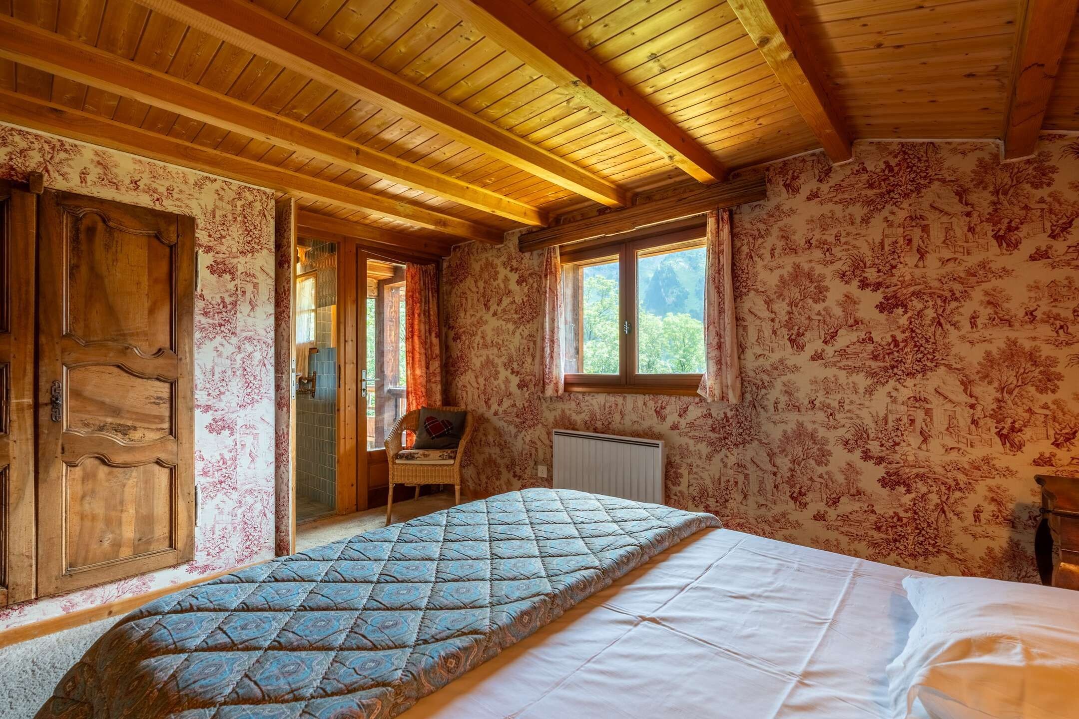 A wooden room with a bed, a chair, and a window.
