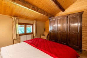 Ein Schlafzimmer mit Holzboden, einem großen Bett mit roter Decke, einem Holzschrank und einem Fenster mit Vorhängen.