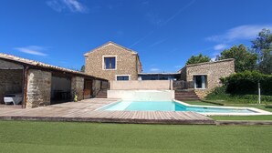 Un bâtiment en pierre doté d’une piscine, d’une terrasse en bois et d’une pelouse verdoyante.