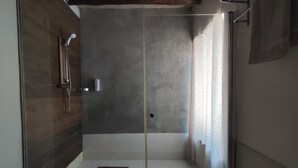 Une douche à l’italienne avec une porte en verre, un banc en bois et un sol carrelé.
