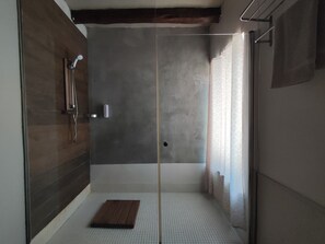 A walk-in shower with a glass door, a wooden bench, and a tiled floor.