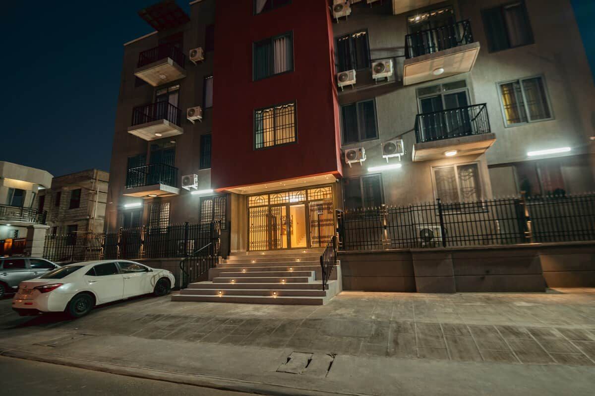 A multi-story building with a red facade, multiple balconies, and a staircase leading to the entrance.