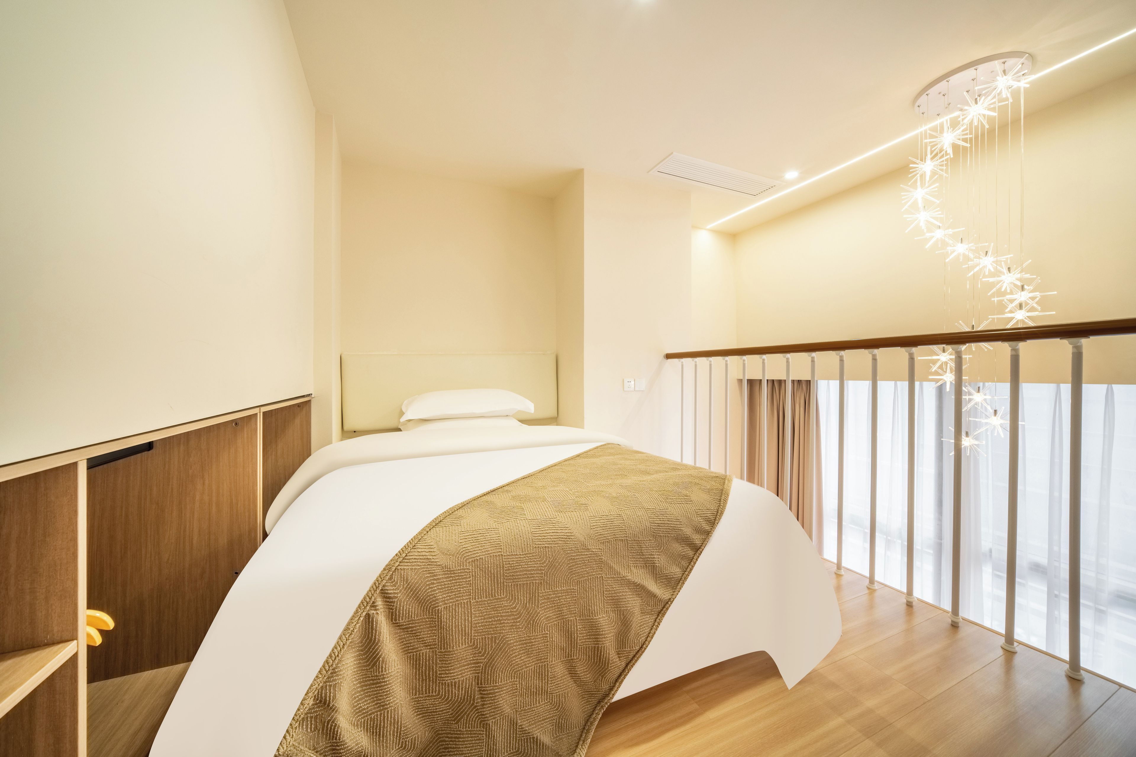 A hotel room with a bed, wooden floor, a ceiling light fixture, and a window with curtains.
